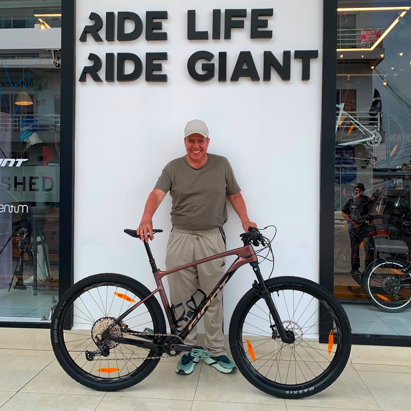 Cliente con su nueva bicicleta de montaña Giant color vino frente al mural Ride Life Ride Giant