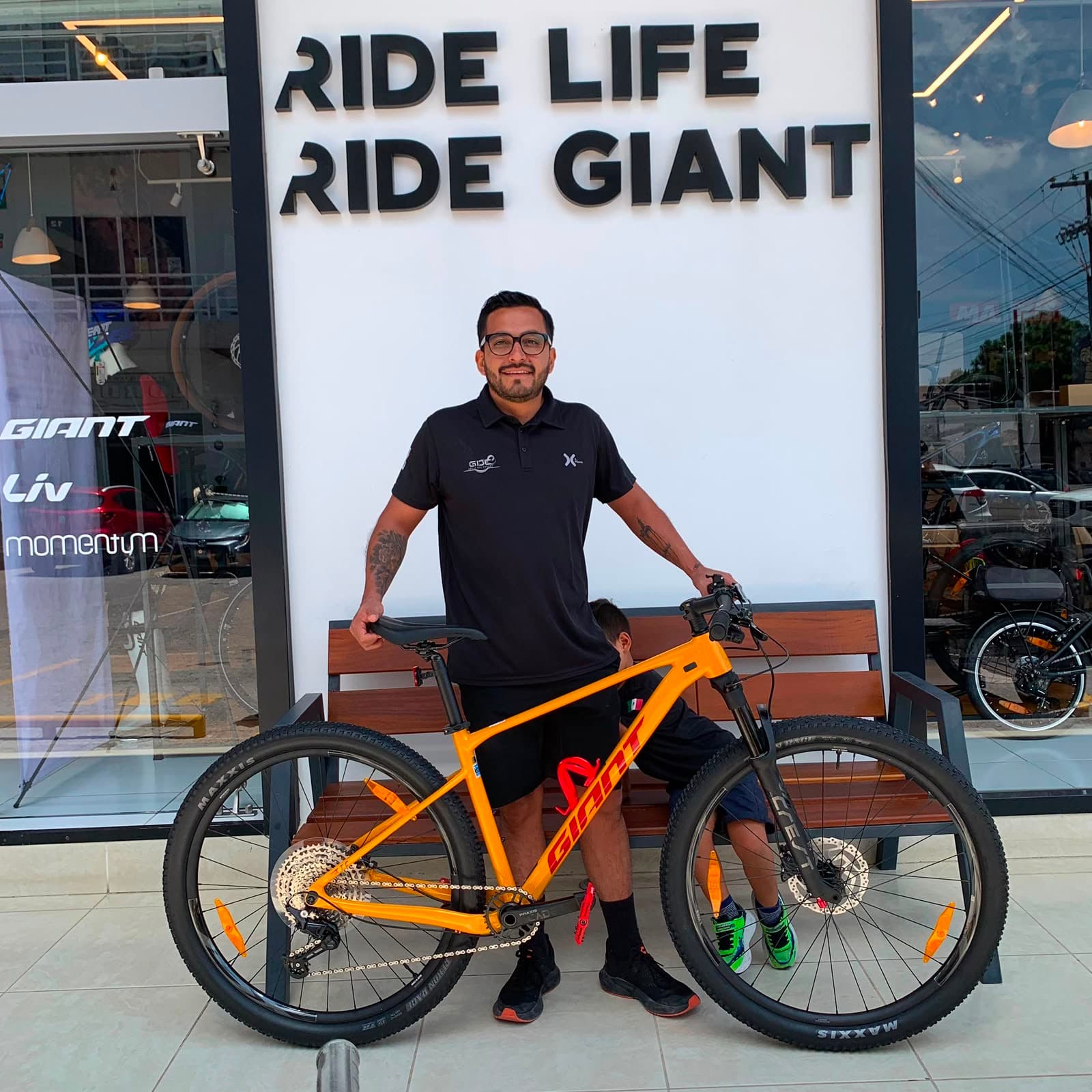Cliente con su nueva bicicleta de montaña Giant naranja frente al mural Ride Life Ride Giant