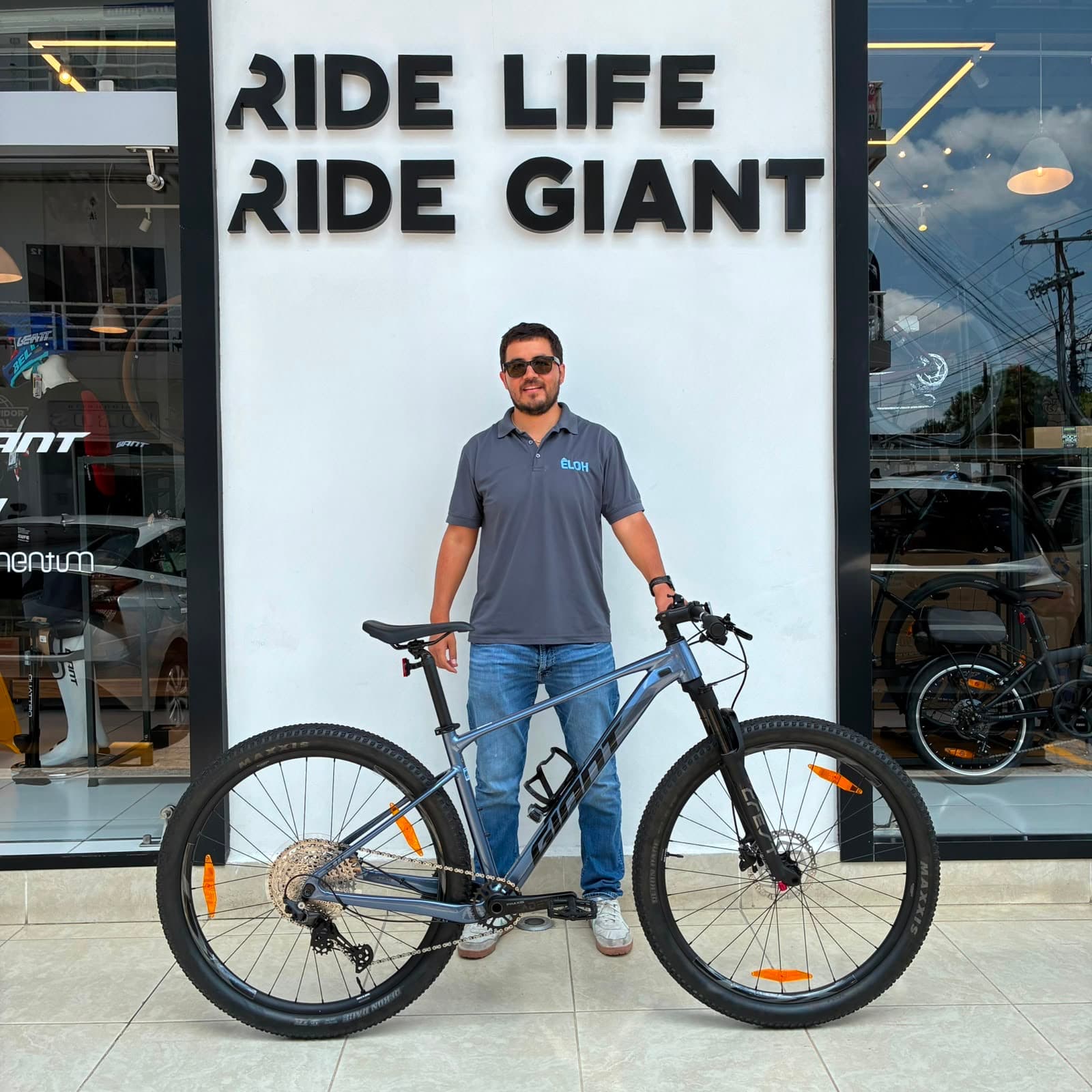 Cliente con su nueva bicicleta de montaña Giant gris frente al mural Ride Life Ride Giant