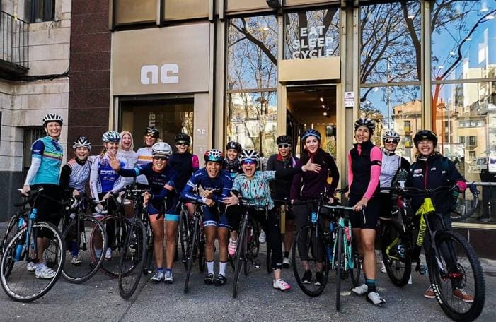 Grupo de mujeres ciclistas reunidas con sus bicicletas frente a una tienda