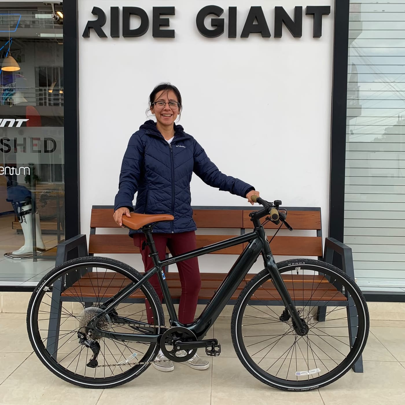 Cliente con su nueva bicicleta urbana Giant negra de sillín café frente al mural Ride Giant