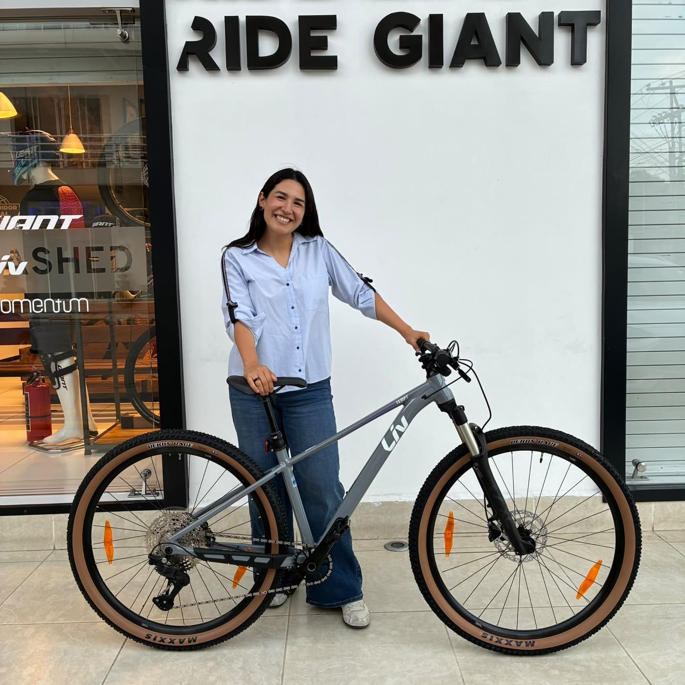 Cliente con su nueva bicicleta de montaña Liv gris de llantas banda café frente al mural Ride Giant