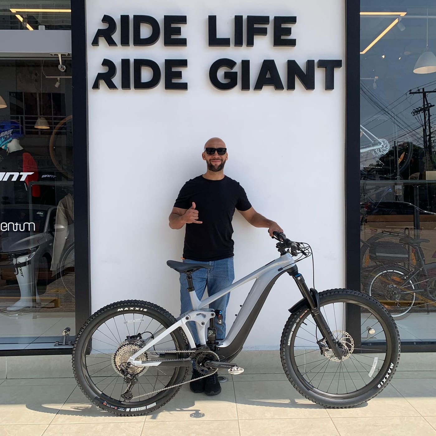Cliente con su nueva bicicleta Giant de doble suspensión plata frente al mural Ride Life Ride Giant
