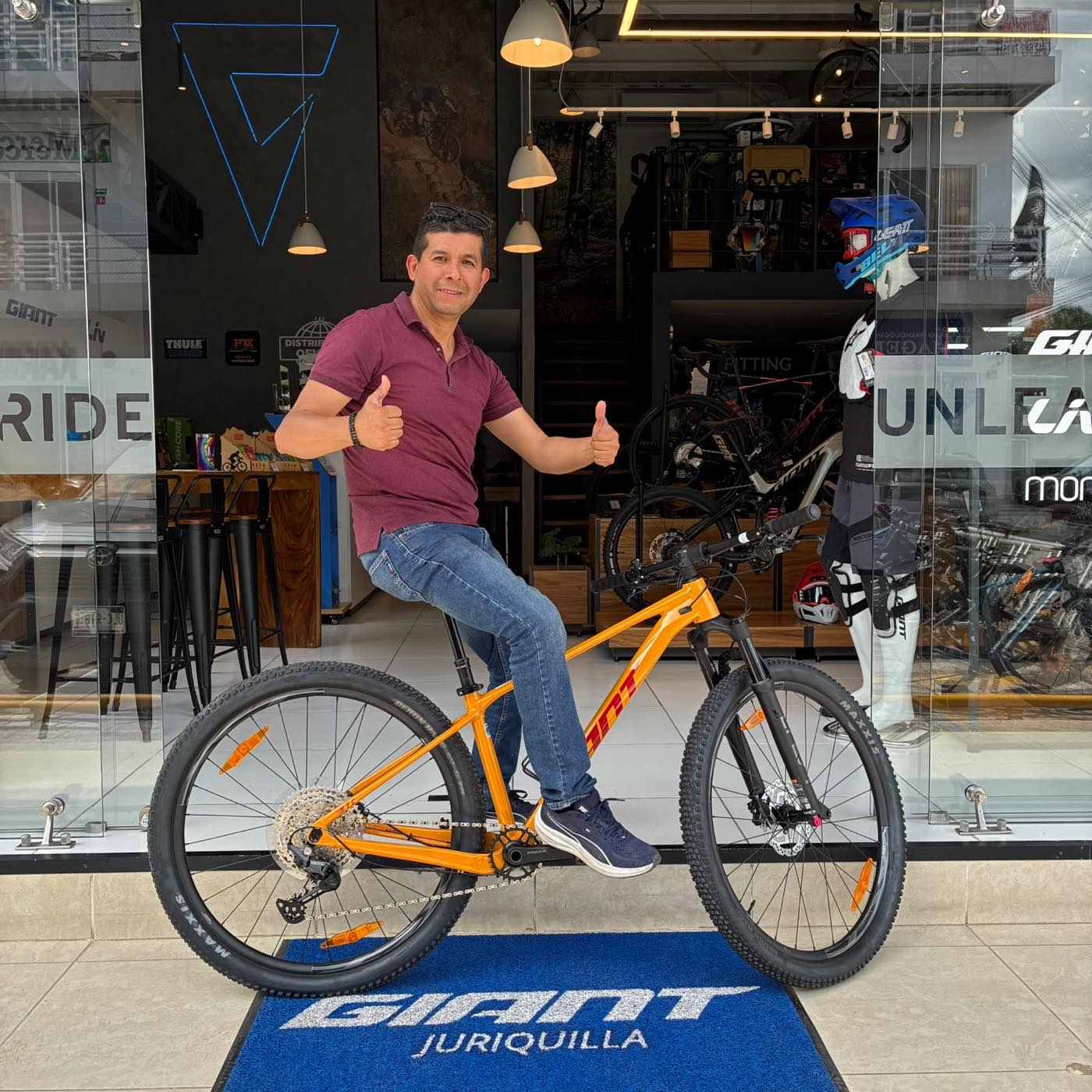 Cliente sentado en su nueva bicicleta de montaña Giant naranja en el ventanal de la tienda