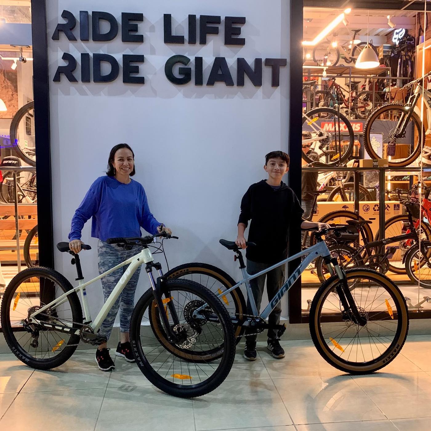 Dos clientes con sus nuevas bicicletas de montaña Giant frente al mural Ride Life Ride Giant