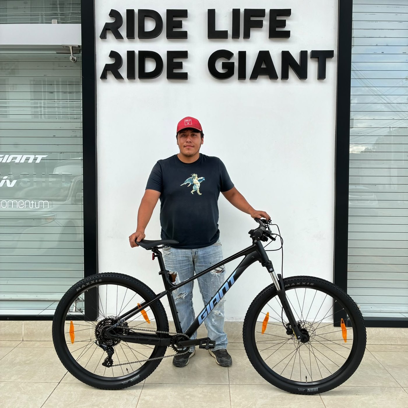 Cliente con su nueva bicicleta de montaña Giant negra frente al muro Ride Life Ride Giant