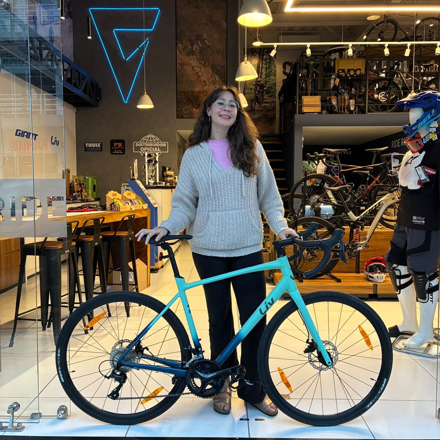 Clienta con su nueva bicicleta de ruta Liv turquesa bajo el neón de la tienda