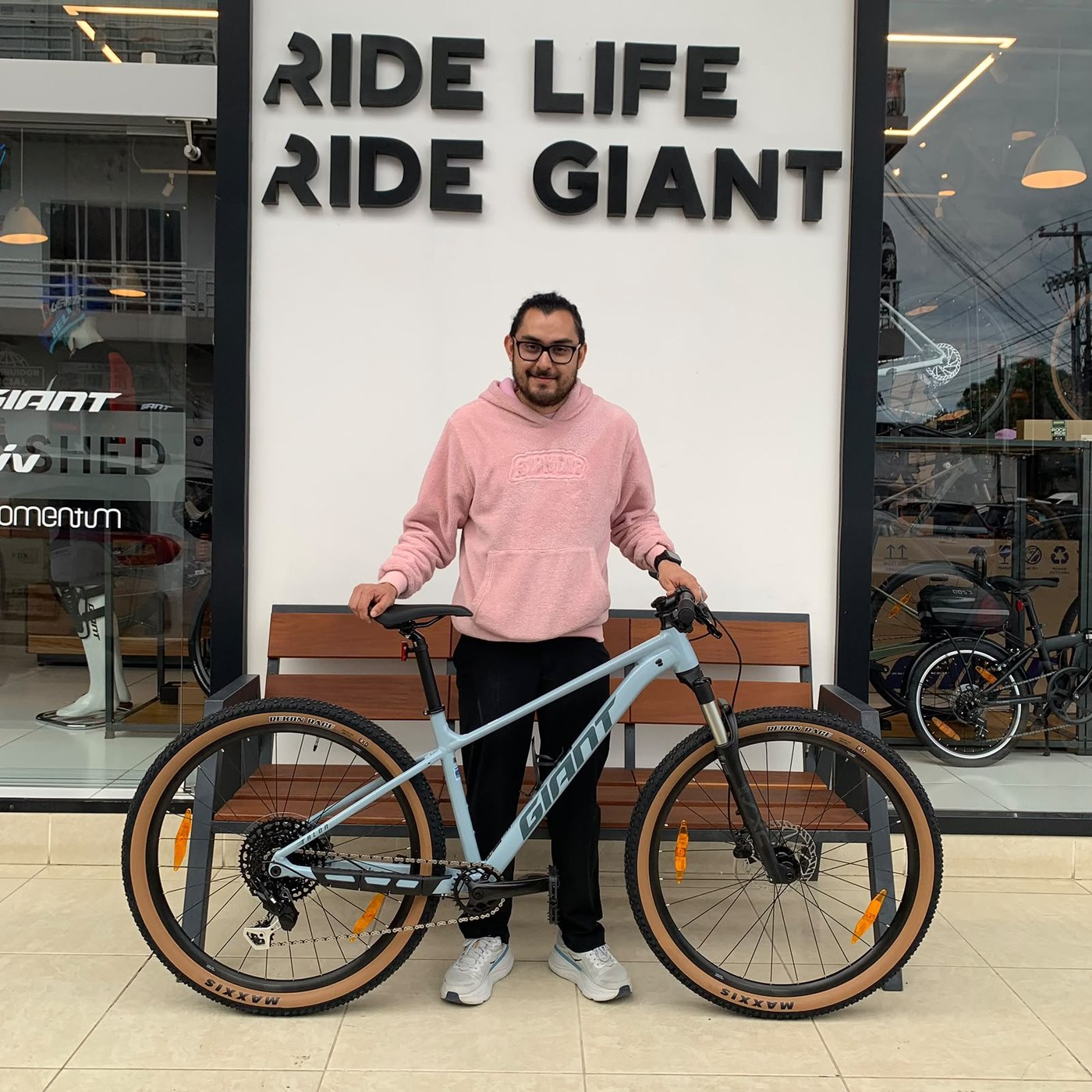 Cliente con su nueva bicicleta de montaña Giant azul claro frente al muro Ride Life Ride Giant