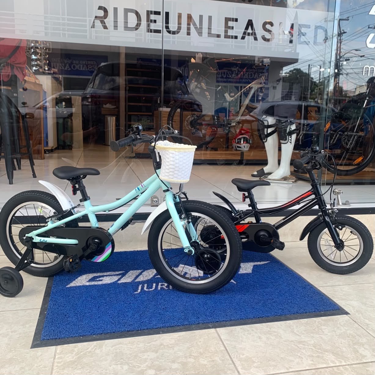 Dos bicicletas infantiles, una Liv turquesa con canasta y una negra, sobre el tapete de Giant Juriquilla