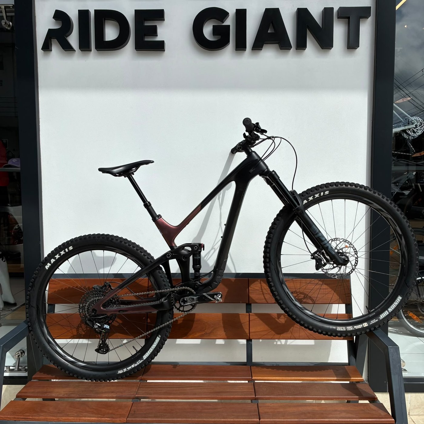 Bicicleta de montaña Giant de doble suspensión negra sobre la banca, frente al muro Ride Giant